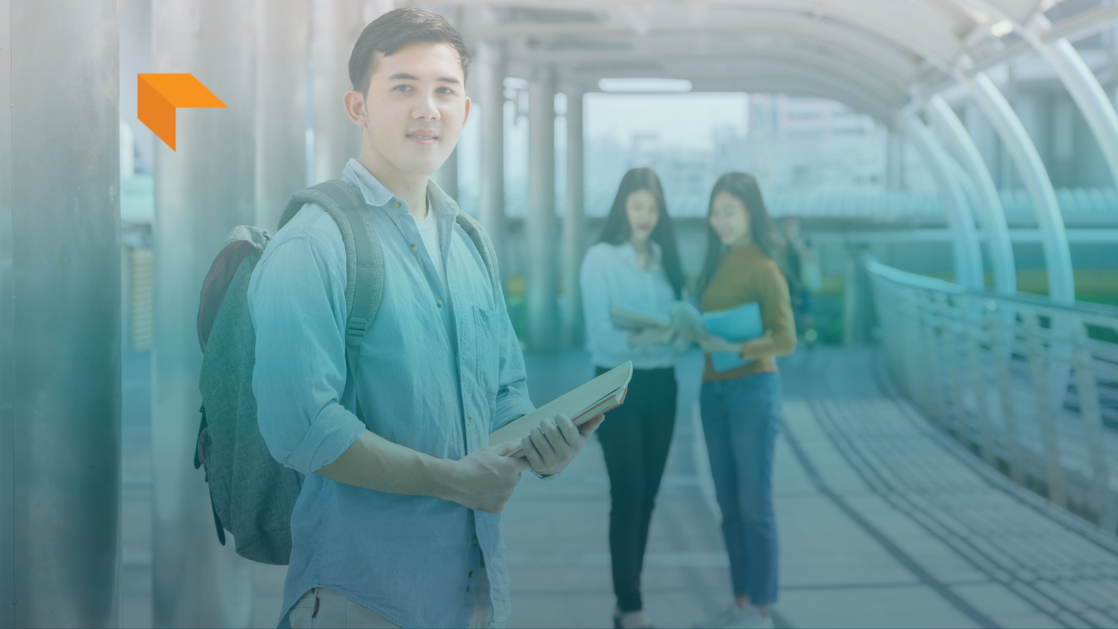 A young East Asian male student wearing a light blue denim shirt and backpack, holding books and looking directly at the camera with a subtle smile. In the blurred background, two female students stand together on a modern covered pedestrian bridge or walkway. An orange stylized arrow logo appears in the top-left corner, and a blue-to-light gradient overlay spans across the image.