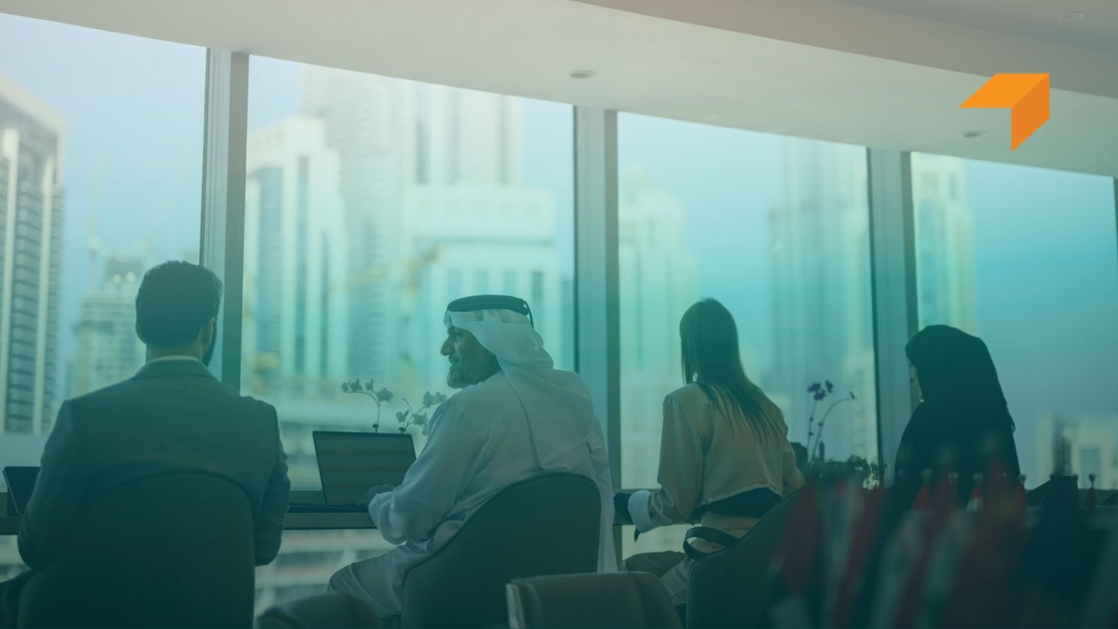 Diverse group of UAE business professionals, including an Emirati man in traditional attire, working on laptops in a modern office overlooking modern city skyscrapers.